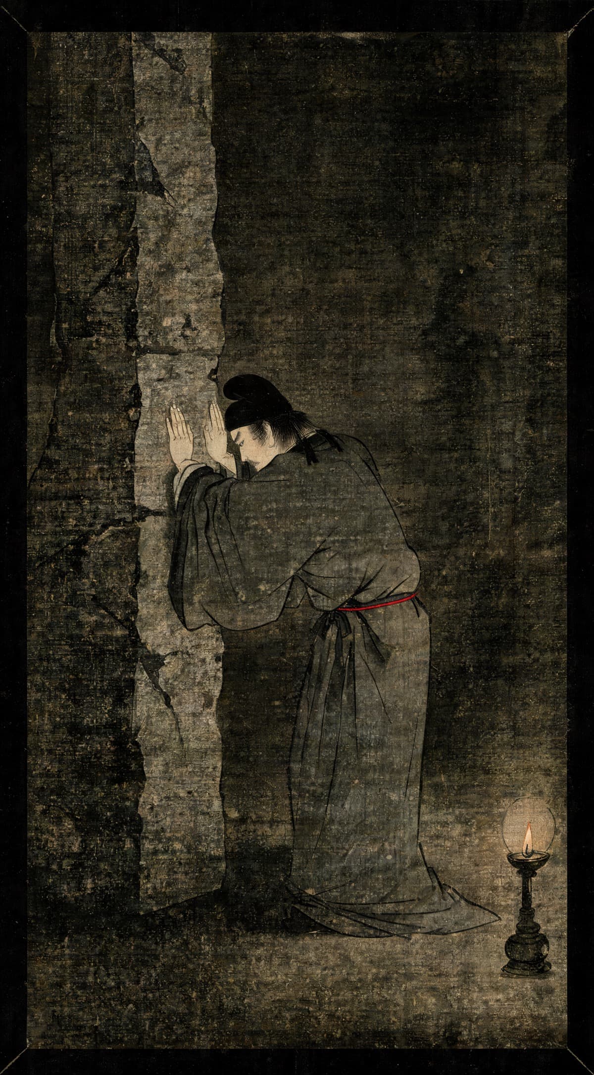Painting of a robed figure braced in a static press against a stone wall, both palms flat, beside a single oil lamp