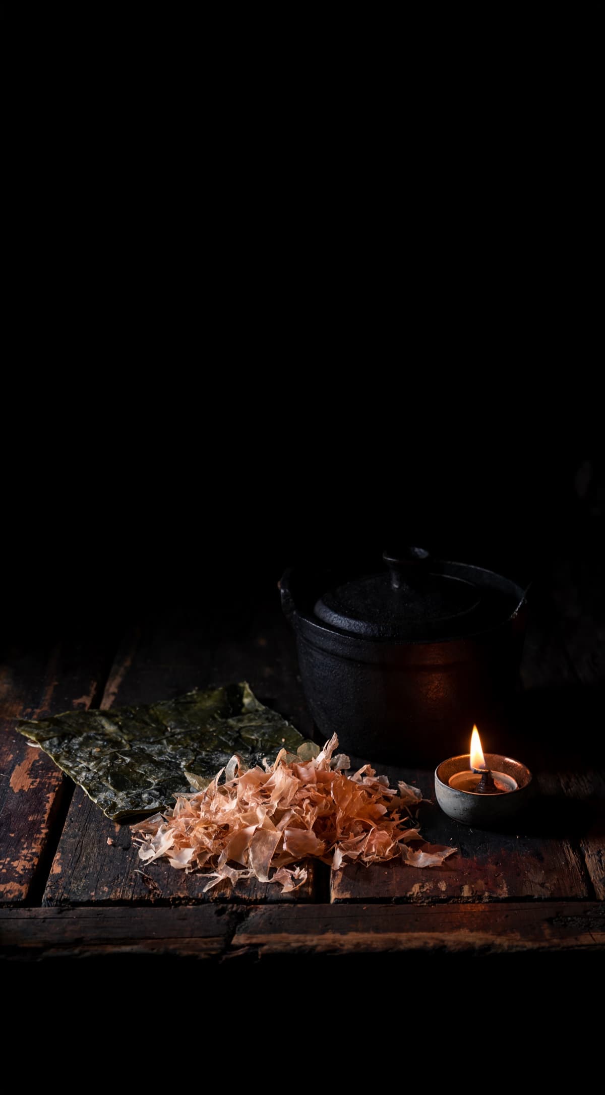 Dashi — The base stock, lit by a single flame in a dark kitchen